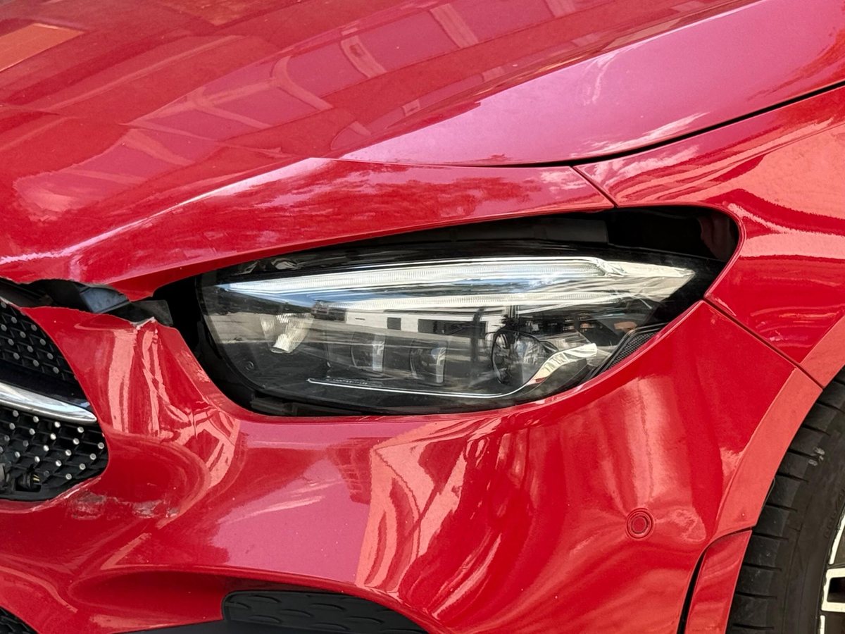 Close-up: torn bumper corner and damaged headlight on a red Mercedes