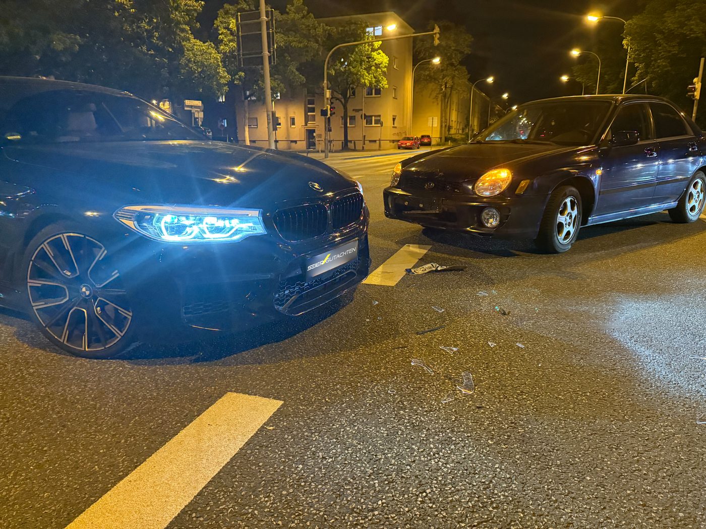 Accident scene at night: BMW and Subaru after a collision at an intersection, broken glass on the road