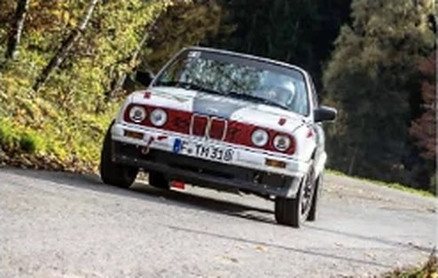 BMW E30 Rallyefahrzeug in Frontansicht auf Asphalt im Wald